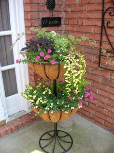 three tiered planter with flowers in front of a brick wall and welcome sign