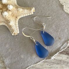 These gorgeous and luminescent sapphire blue sea glass drops are hand wired in our "perfectly imperfect" nest wrap style onto sterling silver hooks with rubber safety backs for added security. Each piece of sea glass is unique and may vary in shape and size, but they are all approximately one inch long. These earrings are not only beautiful but also lightweight and comfortable to wear. They are the perfect gift for any ocean or mermaid lovers on your list. Toes in the sand, sunshine above... my beach soul is happy!     Earrings dangle 2 inches (please see photo).     Recycled, cultured sea glass pebbles in sapphire blue. Please allow for slight difference in size and shape.     Sterling silver hooks with rubber safety nuggets.     Gift ready. Your earrings come in an eco friendly muslin gi Glass Pebbles, Mermaid Lover, Sea Glass Earrings, Ocean Jewelry, Blue Sea Glass, Sapphire Blue, Perfectly Imperfect, Glass Earrings, Earrings Dangle