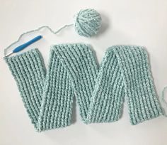 two knitted mitts next to a ball of yarn and a crochet hook