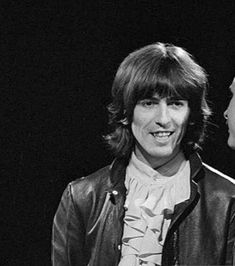 two men standing next to each other in front of a black background and one is wearing a leather jacket