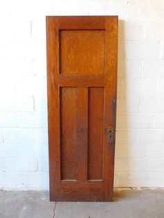 an old wooden door is shown against a white brick wall and concrete floor, with the bottom panel missing