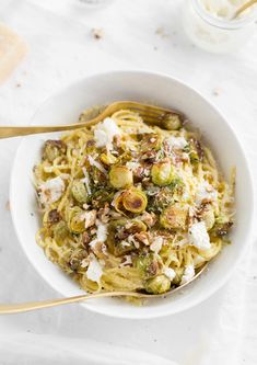 a white bowl filled with pasta covered in toppings and topped with parmesan cheese