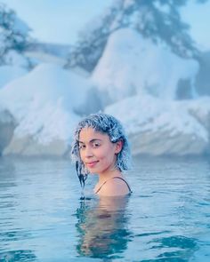 a woman with blue hair is in the water near some snow covered mountains and rocks