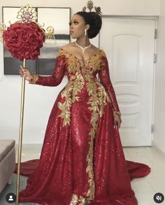 a woman in a red and gold gown holding a large rose with an elaborate crown on her head