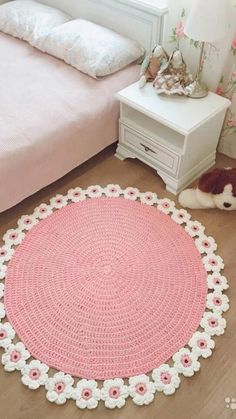 a crocheted round rug is on the floor in front of a bed with a teddy bear