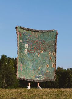 a person standing in the grass holding up a large piece of cloth with sunflowers on it