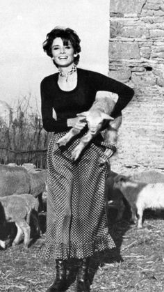 an old photo of a woman standing in front of some animals and holding something up to her chest