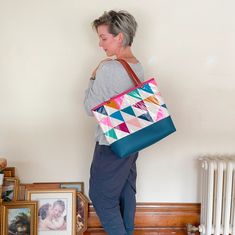 a woman carrying a colorful tote bag in front of a wall with pictures on it