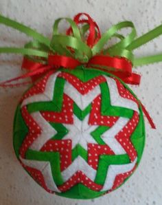 a green and red ornament hanging on a wall with ribbon around it's edge