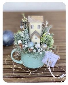 a small house in a teacup filled with greenery and christmas decorations on a wooden table