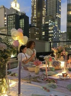 two women sitting at a table with plates and candles in front of the city skyline