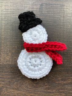 a crocheted snowman sitting on top of a wooden table next to a red and black scarf