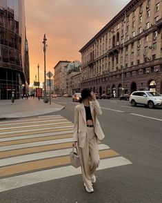 a woman is walking down the street with her hand on her head and wearing a tan suit