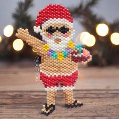 a beaded santa clause figurine is posed on a wooden table with christmas lights in the background