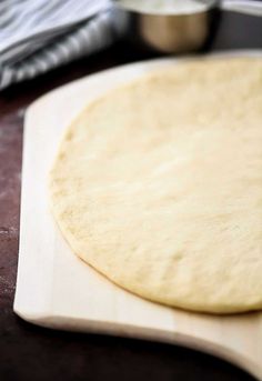 an uncooked pizza dough sitting on top of a wooden cutting board