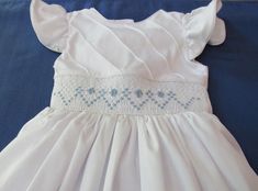 Adorable dress with hand smocked bodice. Hand smocked in the front of the bodice only, embroidered flowers. MADE TO ORDER Pristine white on white, with ruffled angel sleeves. Snapped closure in back. For custom orders allow 2-3 weeks for delivery. Fitted Dress With Smocked Bodice For Baptism, Fitted Light Blue Smocked Dress With Smocked Cuffs, Light Blue Fitted Smocked Dress With Smocked Cuffs, Spring Wedding Dress With Smock Details, White Fitted Smocked Dress For Baptism, Spring Wedding Smocked Dress With Smocked Bodice, Light Blue Smocked Dress With Ruffles And Fitted Style, Summer Baptism Smocked Dress With Smocked Back, Fitted Smocked Dress For Baptism In Summer