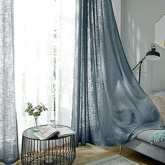 a living room filled with furniture and a window covered in blue sheer curtaining next to a coffee table