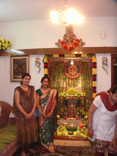 three women are standing in front of a decorated stage with flowers and garlands on it