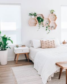 a bedroom with white bedding and wooden shelves on the wall, potted plants