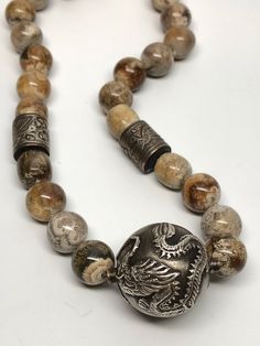 Wonderful necklace with a large silver bead feature 2 Chinese dragons. There are also 2 barrel shaped silver beads with birds and flowers on them. The stone beads are a brown and beige agate, each one is unique with swirls of different colors. The clasp is a large oval marked sterling. Each bead is hand knotted. The barrel silver beads have some copper showing through, otherwise in great condition. Necklace measures 14 inches long. Dragon bead measures approximately 1 inch in diameter. Agate bea Silver Agate Jewelry With Large Beads, Silver Agate Beaded Necklace, Silver Agate Beaded Necklaces With Polished Beads, Silver Agate Beaded Necklace With Polished Beads, Artisan Silver Agate Beaded Necklace, Silver Agate Beaded Necklaces With Round Beads, Unique Silver Beads With Natural Stones, Chinese Dragons, Handmade Ceramic Jewelry