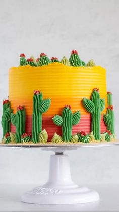 a cake decorated with green, yellow and red frosting cactuses on a white pedestal