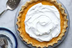 a pie with whipped cream on top sitting next to a fork and bowl full of dessert