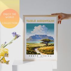 a person holding up a poster in front of a vase with flowers on it and the text enjoy the world table mountain