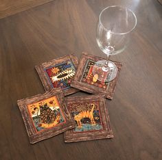 four coasters sitting on top of a wooden table next to a glass filled with wine