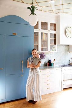 a woman holding a baby in her arms standing next to a blue cabinet and clock