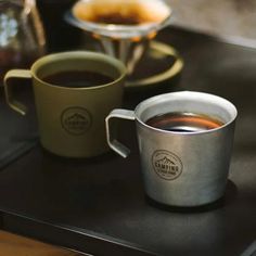 two cups of coffee sitting on top of a black table next to a silver plate