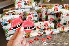 someone is holding up two christmas themed badges in front of some wrapping paper wrapped presents