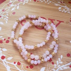 two bracelets with pink beads and gold balls on a wooden table next to flowers