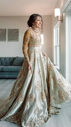 a woman in a long dress standing next to a couch and smiling at the camera