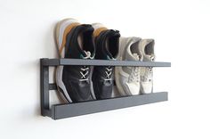 four pairs of shoes are hanging on the wall above a shoe rack with two hooks