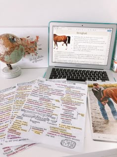 a laptop computer sitting on top of a white desk next to papers and pictures with horses