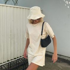 a woman wearing a white hat and dress is walking down the street with her hand on her hip