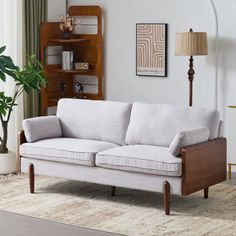 a white couch sitting in a living room next to a wooden book shelf on top of a rug