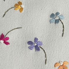 several different colored flowers on a white cloth with stitching in the middle and bottom