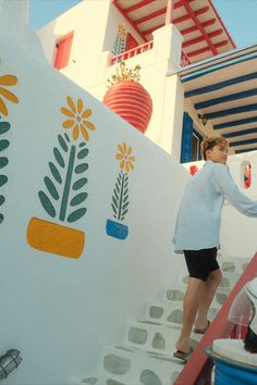 a woman walking up some steps next to a white wall with flowers and plants painted on it