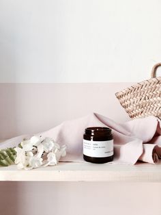 a white shelf topped with a jar of cream next to a wicker basket and flowers