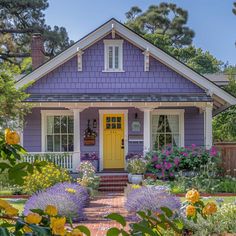 a purple house with yellow doors and flowers in the front yard on a sunny day