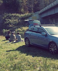 two people sitting on the grass next to a car