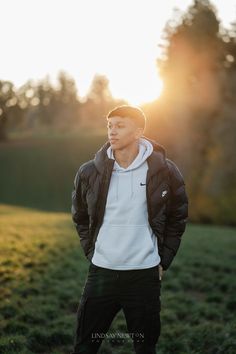 a young man standing in the grass at sunset