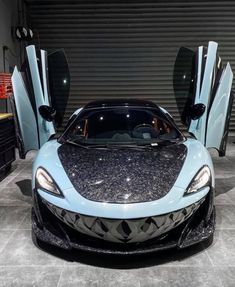 a blue sports car parked in front of a garage door with its doors open to reveal the interior