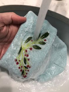 a hand is holding a cloth over a sink faucet that has been decorated with holly leaves and berries