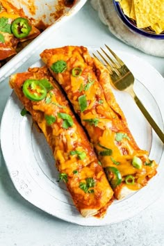 two slices of enchilada on a plate with a fork next to it