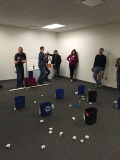 group of people standing in an office area with trash cans scattered on the floor and around them