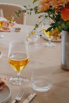 there is a table set with wine glasses and silverware on it, along with flowers in vases