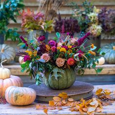 a vase filled with flowers sitting on top of a wooden table next to pumpkins