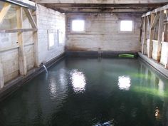 an empty room with water in the floor and windows on the wall, next to a green pool